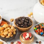 Snack spread on marble countertop with nuts, fruit, puffs, choco